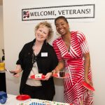 two Clark staff members serving a U.S.-flag decorated cake under a sign that says "Welcome, Veterans"