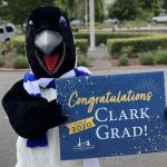 Oswald in a parking lot holding a sign that reads "Congratulations 2020 Clark Grad!"