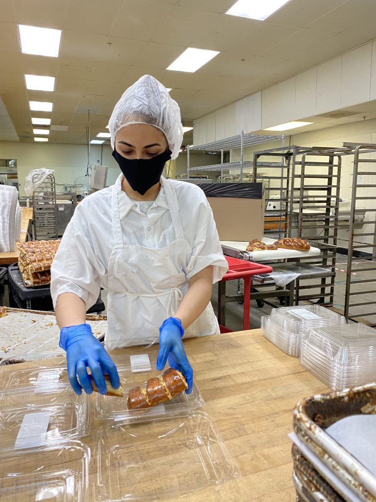 Student in mask and gloves putting baked goods into a plastic to-go container.