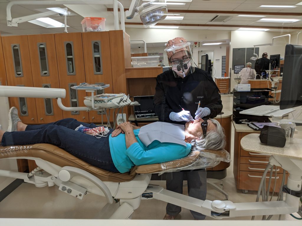 Dental patient lying back in dental chair while dental hygiene student examines her teeth