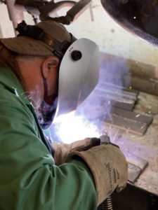 Student in full protective gear welding metal.