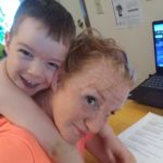 Jessica Bull at her computer with her toddler son on her back