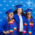 three graduates, two wearing Latinx-themed stoles, pose for a photo against a Clark College backdrop