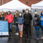 students and staff in masks outdoors in front of tents full of food donations