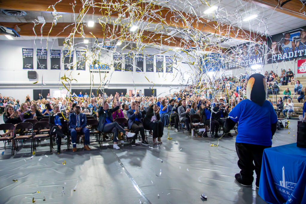 Gym filled with people in chairs and on bleachers while streamers shoot into the audience.