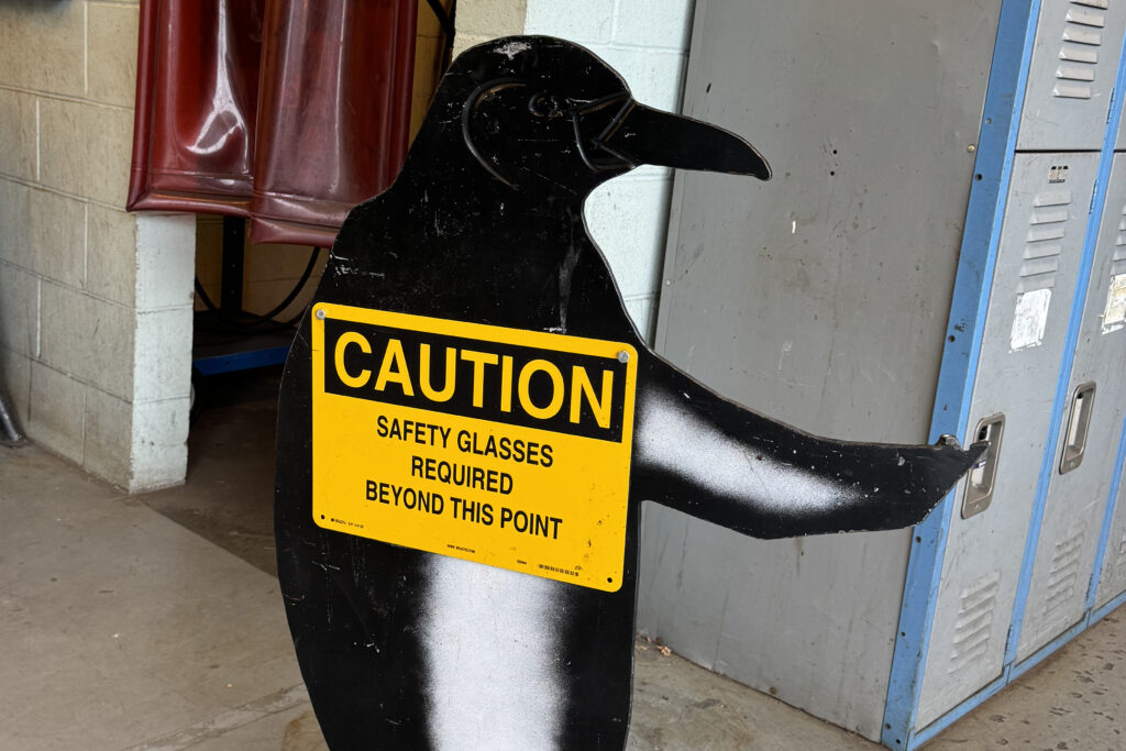 metal penguin with sign "caution safety glasses required beyond this point"