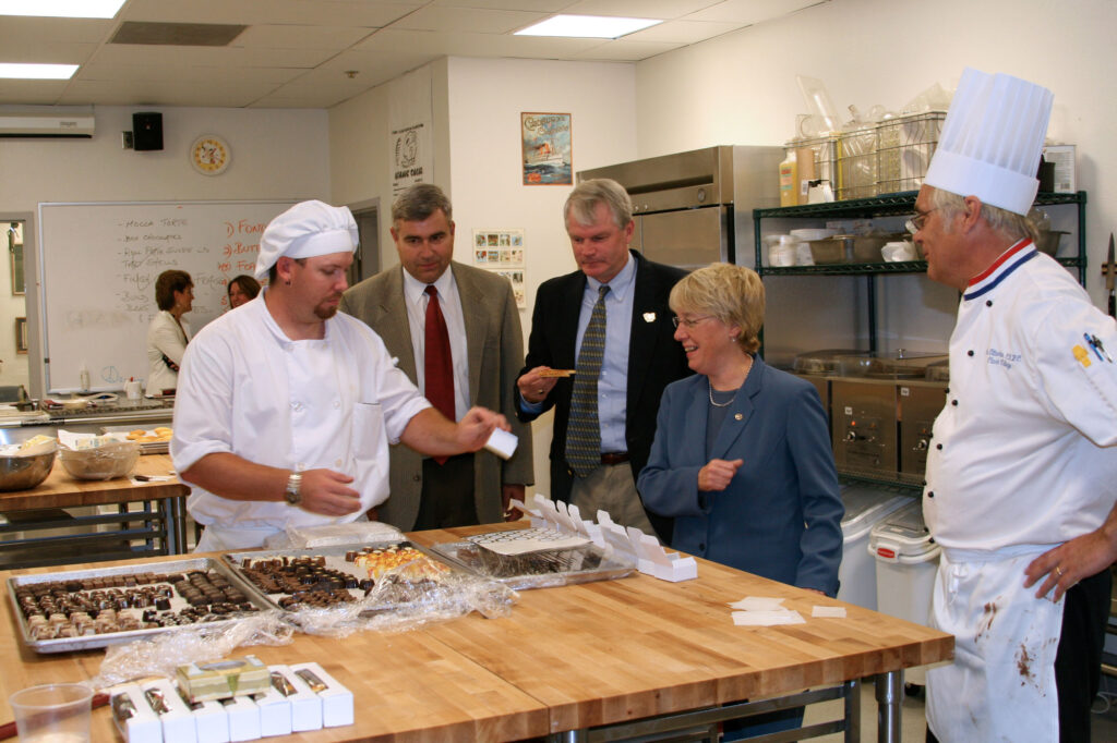 A group of people trying pastries from college bakery, with two individuals wearing chef attire.