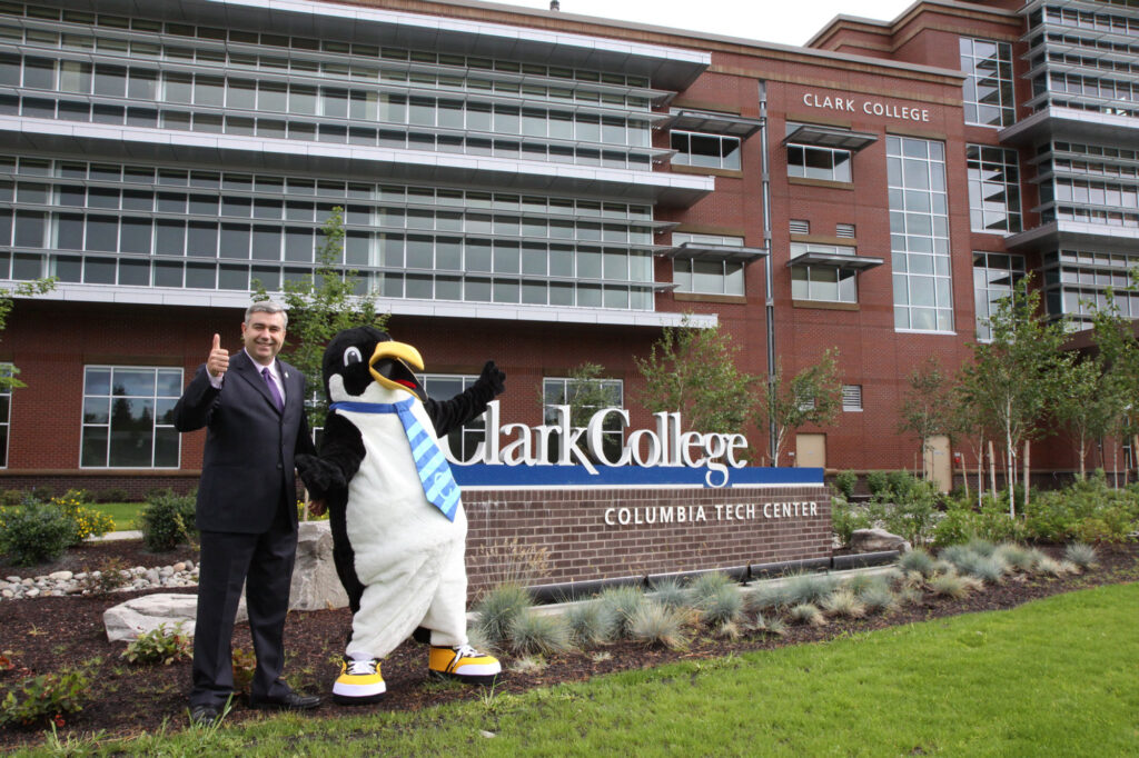 Former Clark President standing with the college's mascot in front of a sign that reads "Clark College Columbia Tech Center".