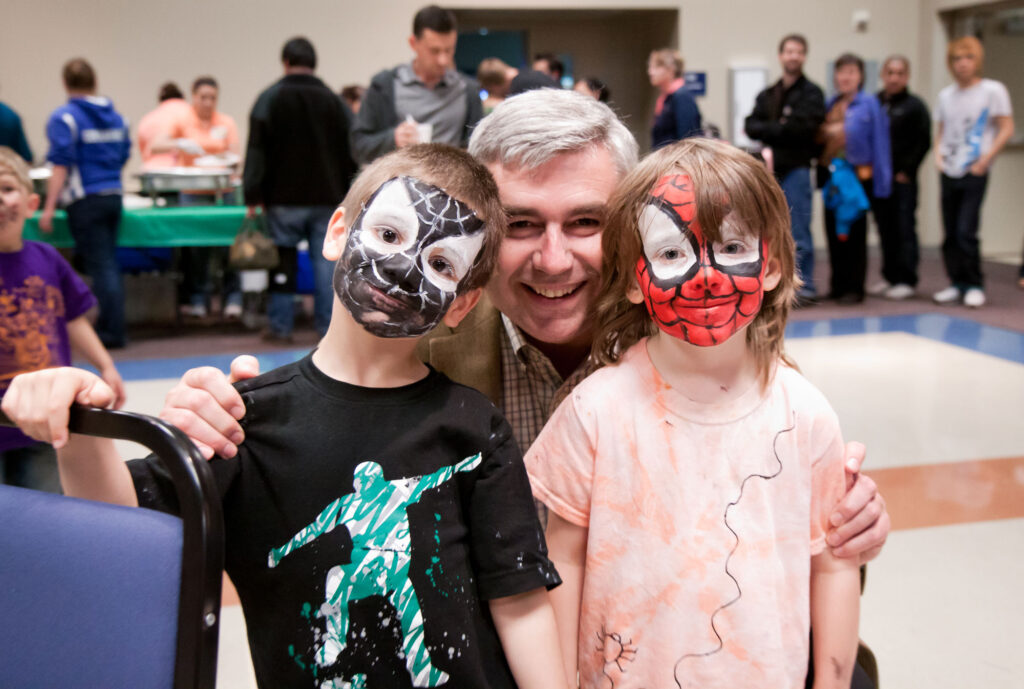 Former Clark College President, Bob Knight, standing with two children who have face paint on.