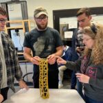 A group of people at a table discussing, with a tower of pasta in the middle.