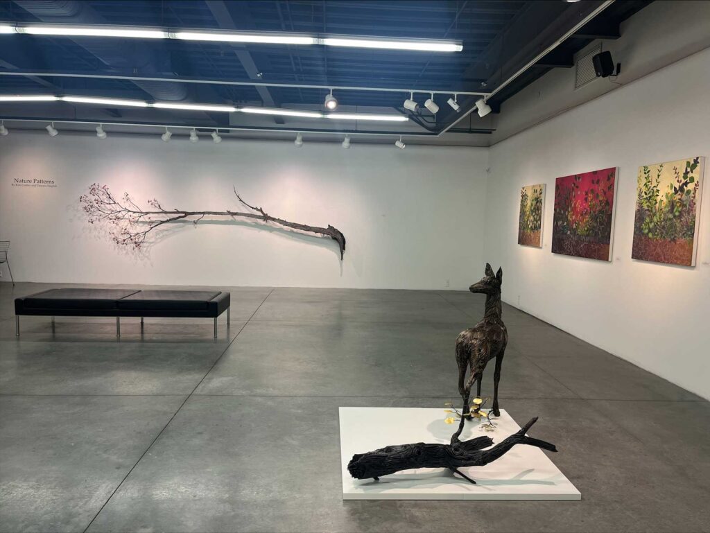 The same art exhibition featuring a tree branch hung on a wall, with the words "Nature Patterns" displayed next to it.