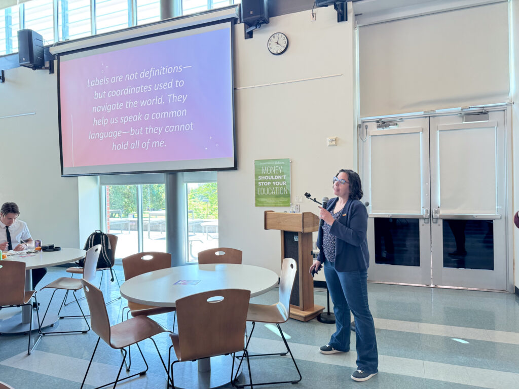 person talks into microphone with large screen to their right.