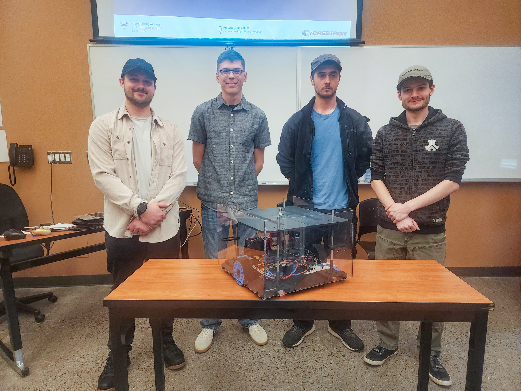 four people stand behind a table with a transparent box