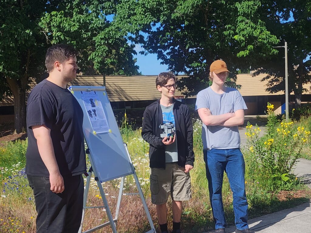 three people stand outside presenting with a small poster.