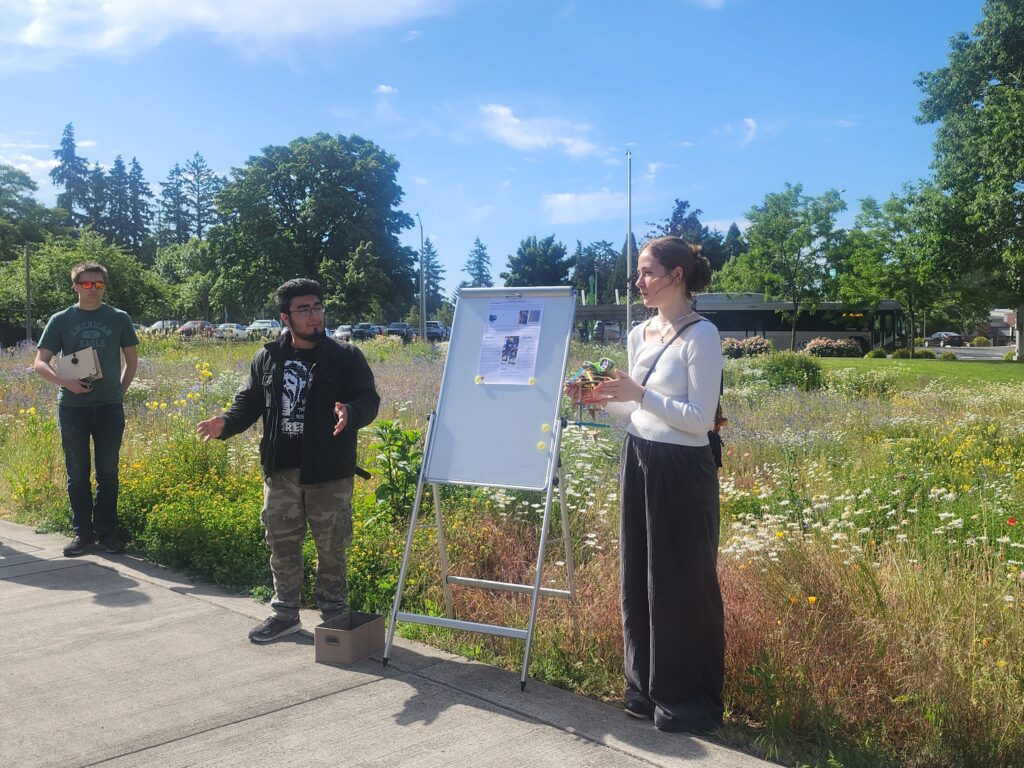 three people stand outside presenting with a small poster.