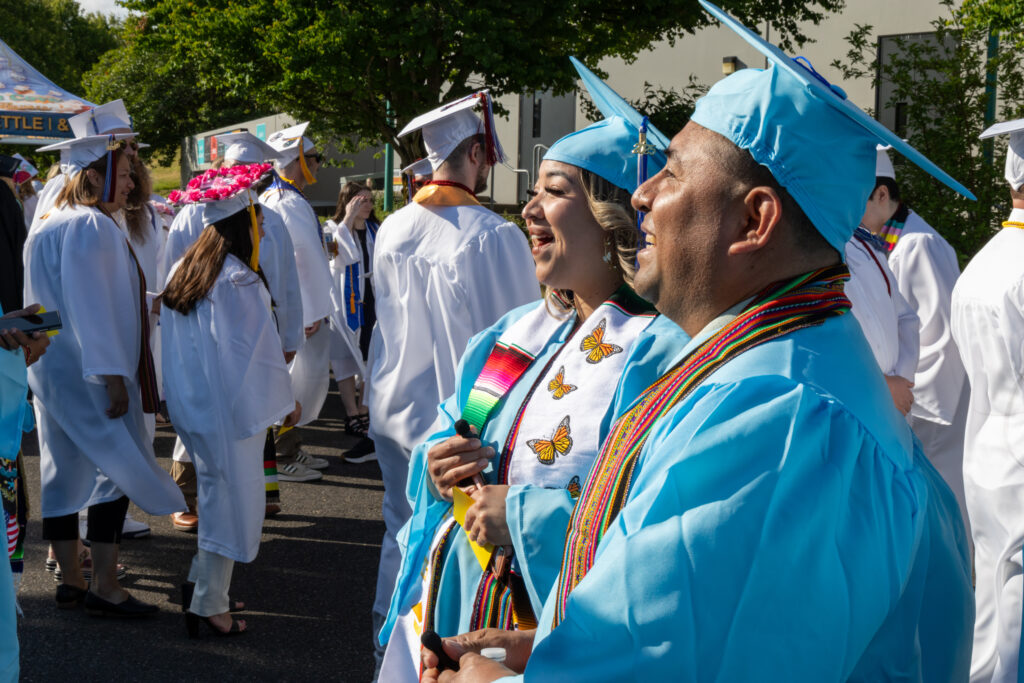 two people in cap and gowns face to the left with other graduates in the background