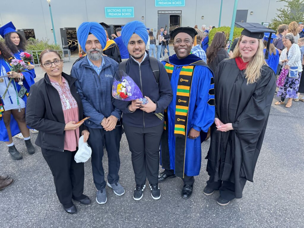 five people stand together three wearing caps and gowns
