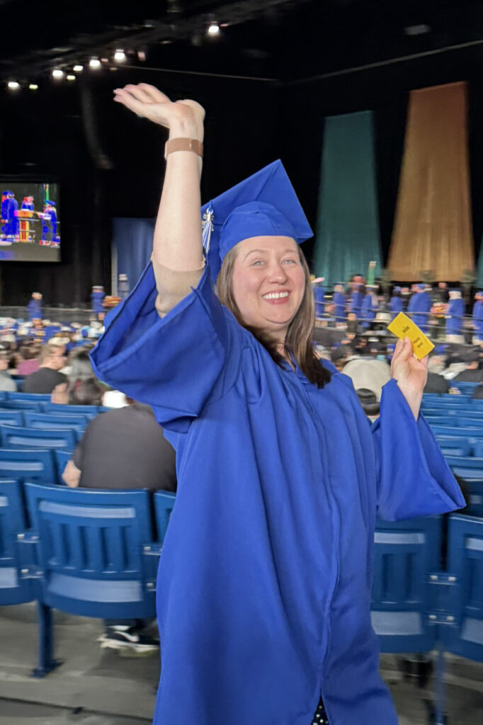 person in cap and gown waves in auditorium