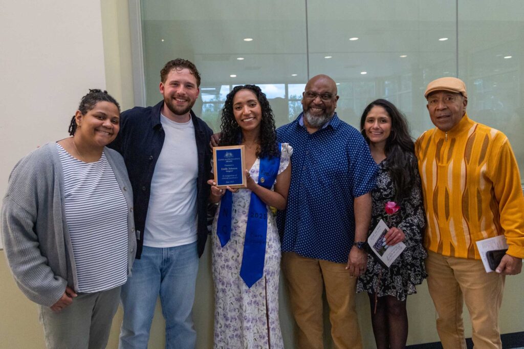 A nursing graduate award winner smiling at the camera, holding her award and standing with her proud family.