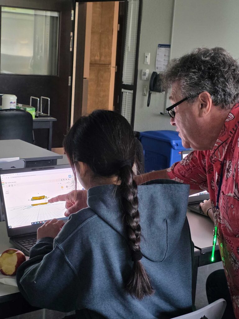 A professor pointing at a laptop screen while a student watches attentively.