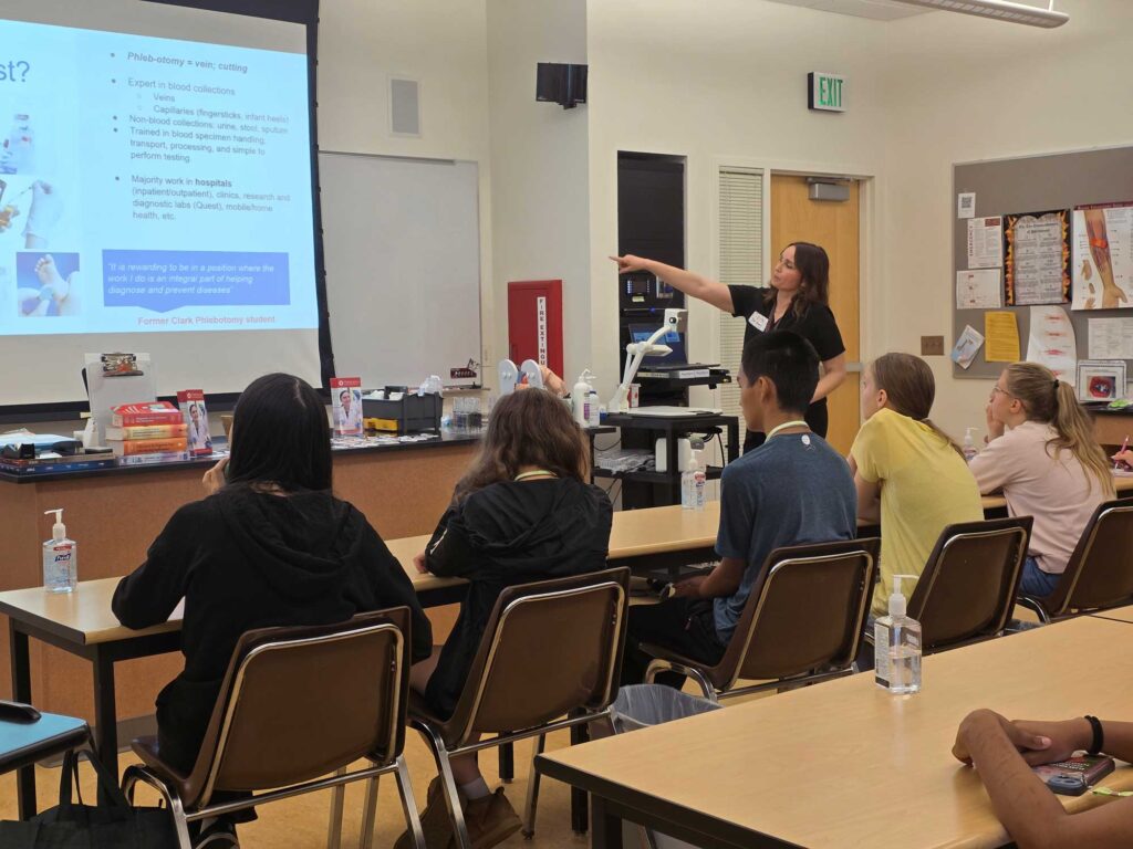 An instructor pointing at a PowerPoint presentation while teaching a group of students.