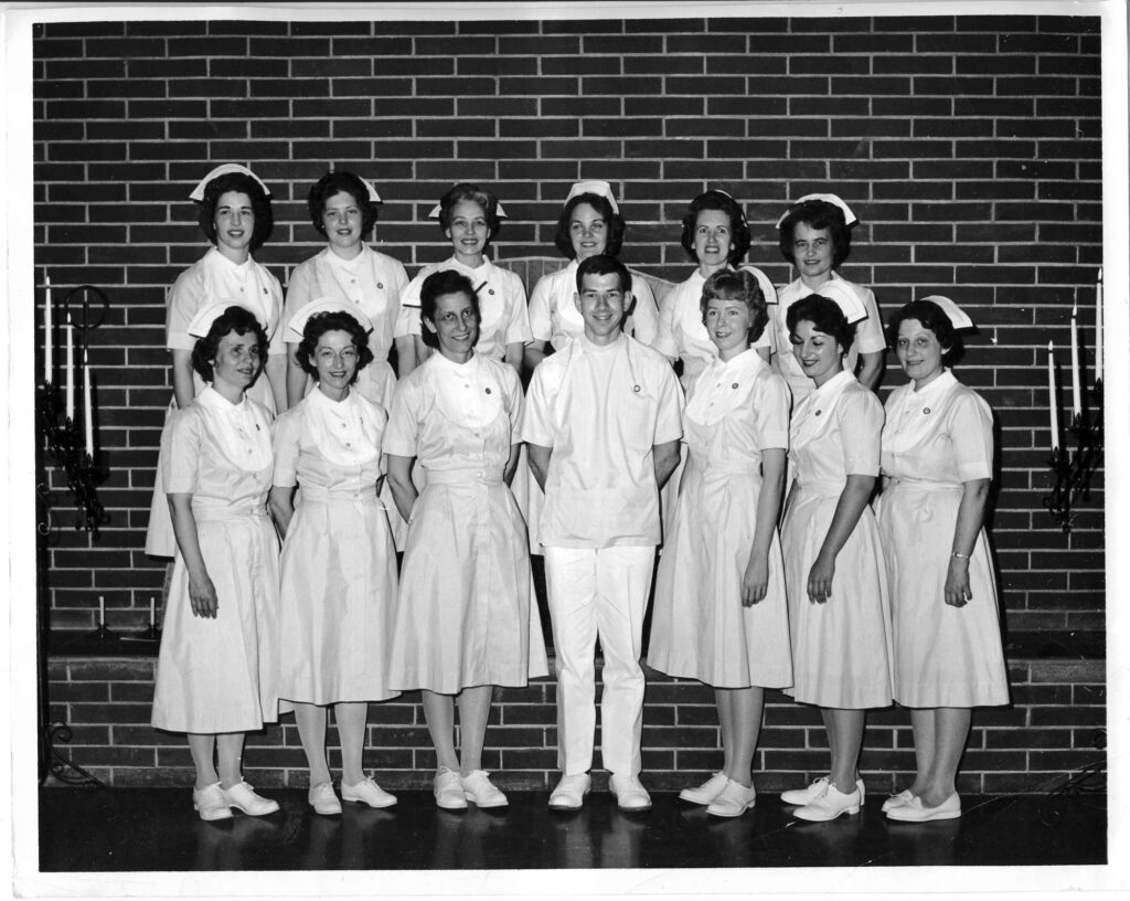 A group of nurses wearing traditional vintage-style nursing uniforms, gathered together for a group photo.